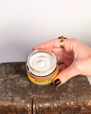 Hand holding a jar of Wrinkle cream - the first wrinkles 35+ Manuka Bio Gerocossen 50 ml on a wooden surface with a neutral background